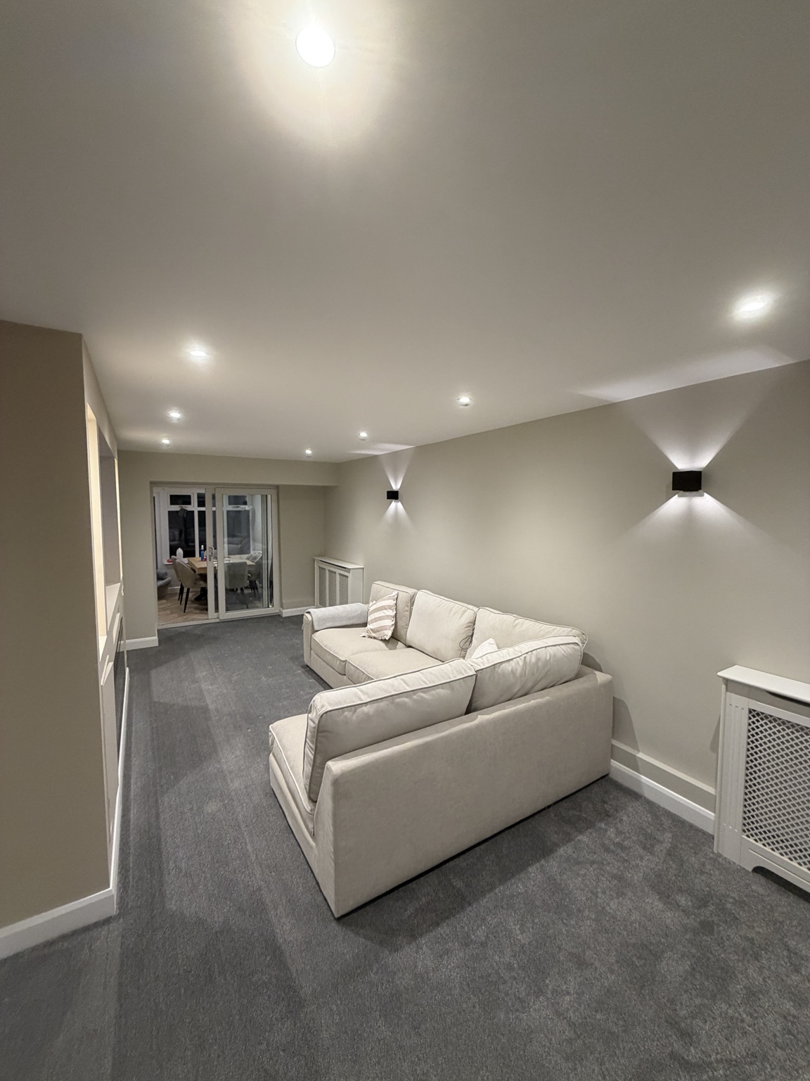 Finished neutral living room with pale sofas, white ceiling and wall lighting